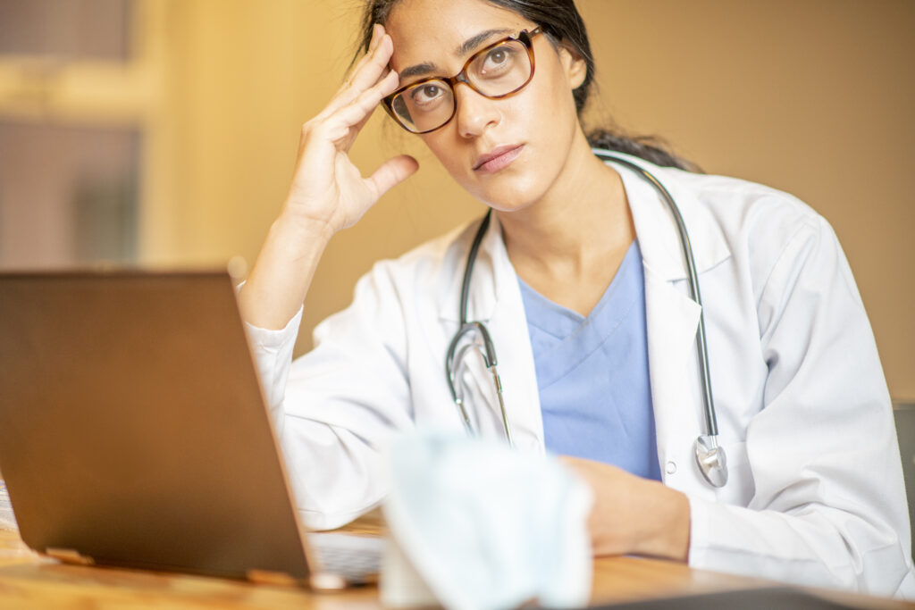 A female doctor is doing an online consultation with a patient using her laptop. She appears to be tired and is resting her head on her hand. Veterinary co-ops can relieve some of this stress.