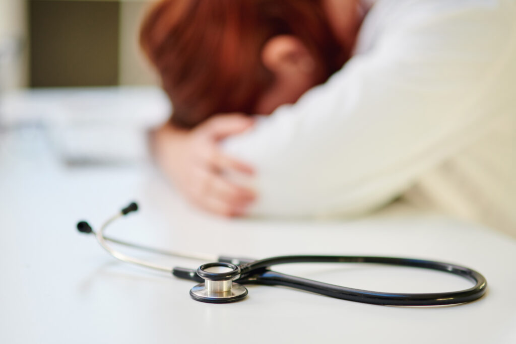 Doctor with head on desk with stethoscope in foreground.