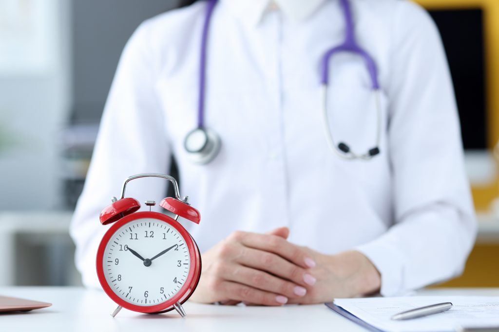 A doctor sits behind a red clock closeup. 