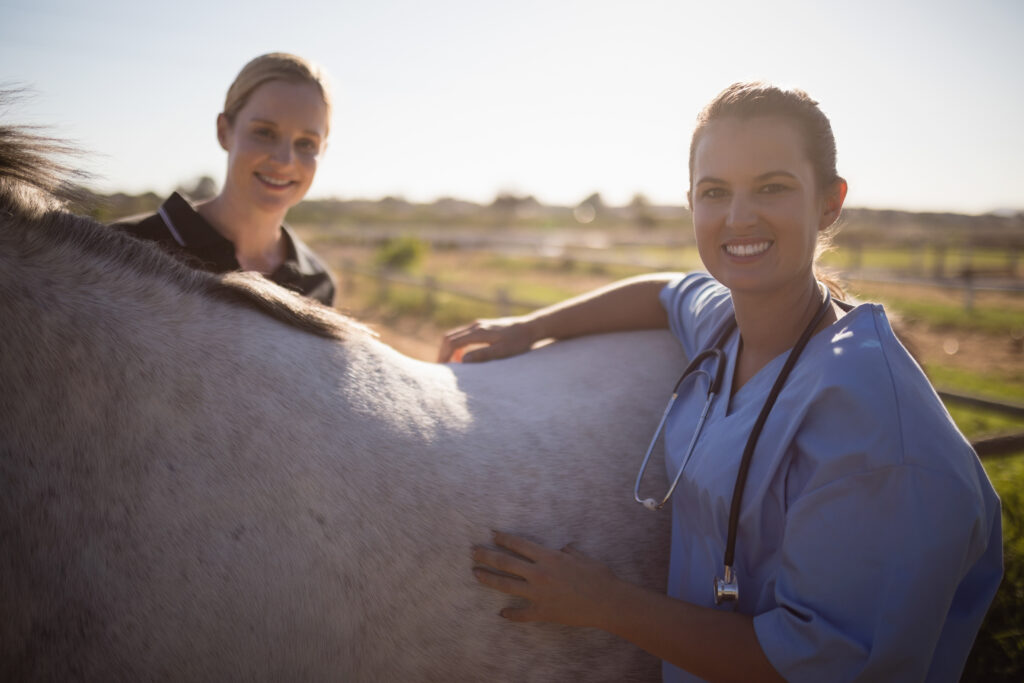 Two early-career veterinarians smiling and standing next to a horse. 