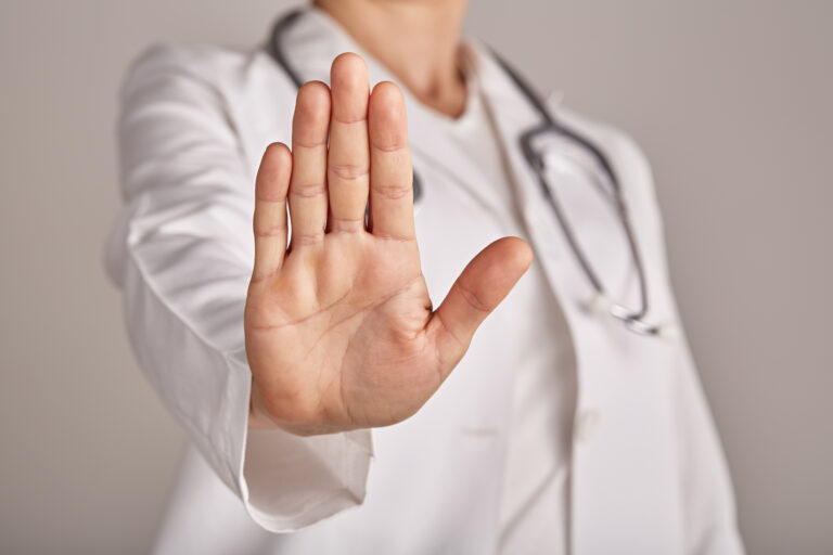 Professional medical doctor in white uniform with a stethoscope around her neck making stop gesture with hand, medicine and healthcare concept