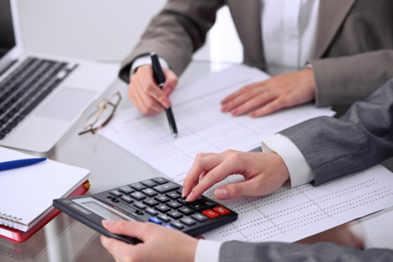 Two female accountants counting on calculator income for tax form completion hands closeup. Internal Revenue Service inspector checking financial document
