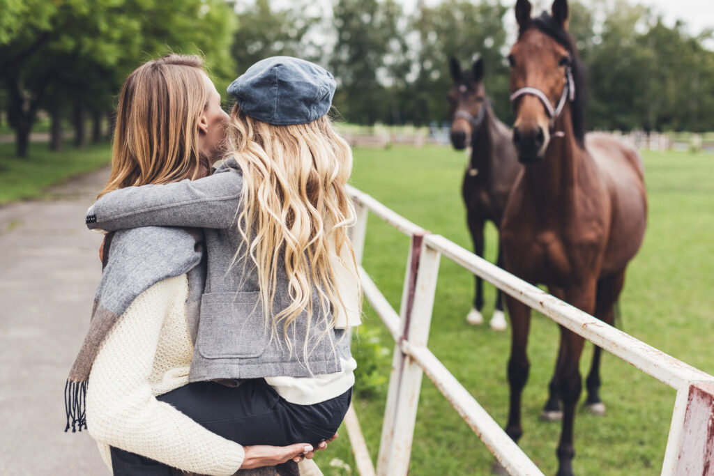 An equine veterinarian parent looking at a horse with child in arms.