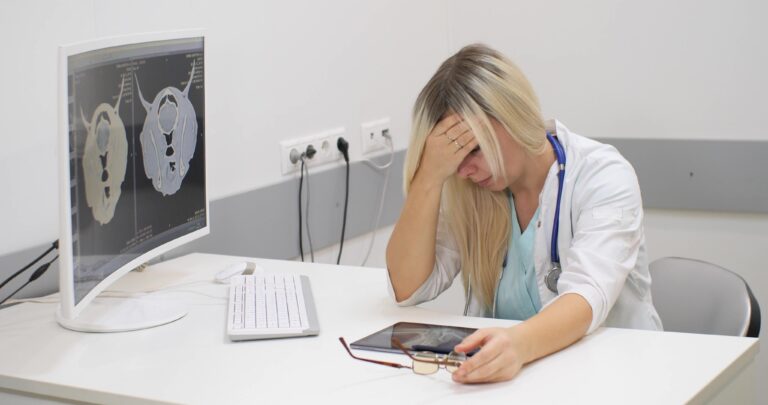The doctor is very exhausted by a lot of work. A woman veterinarian sits at a table resting her forehead on her hand and looks tiredly at the table. The concept of emotional burnout