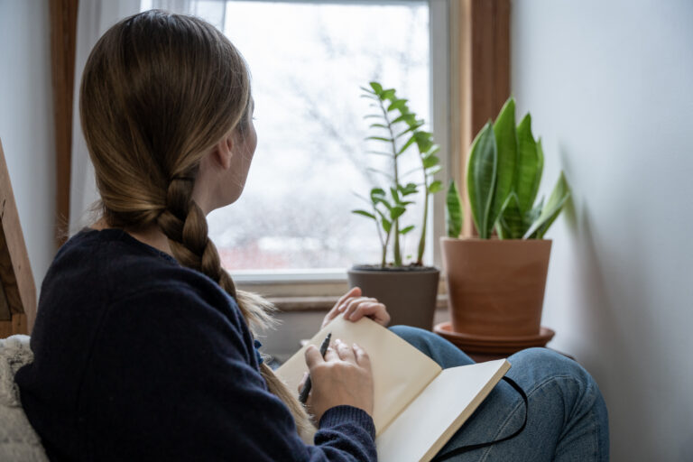 A young woman takes a mental health break to write in a journal at home